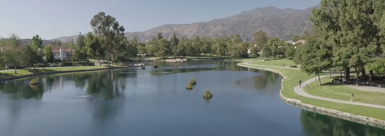 Lago Santa Margarita from the air, homes and the parkway path along the shore, with the dry chaparral ridgeline rising directly behind the city.