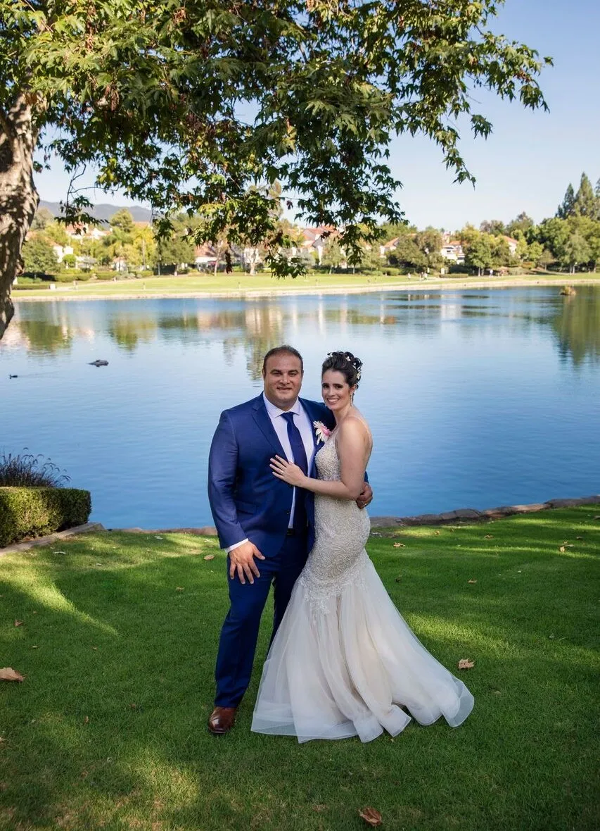 Rod and his wife on their wedding day on the grass at Lago Santa Margarita, the lake and the houses on the far shore behind them.